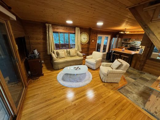 Living room with hardwood floors and log walls, open to the kitchen